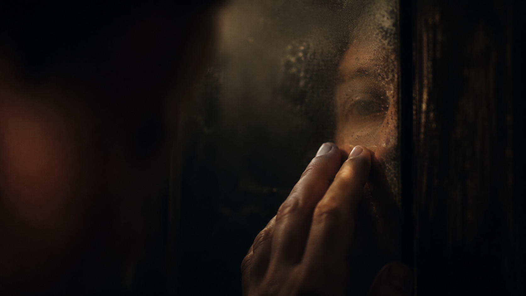 A face reflected in dark glass, matching an essay on self-love and negative self-talk.